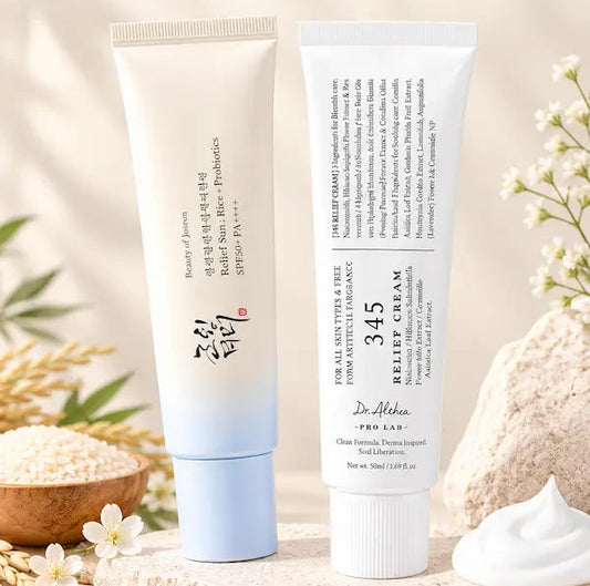 Two skincare tubes from thensmile 'The Korean Glow Duo' displayed on a stone surface with decorative flowers, grains, and a dollop of cream against a warm beige background.